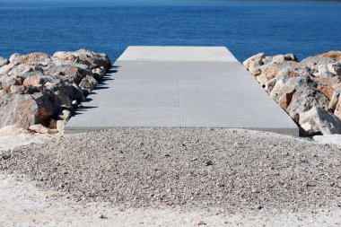 Modern beton iskele, geniş açısal kayalarla çevrili durgun mavi suya dönüşerek mühendislik yapısı ve doğal kıyı şeridi arasında çarpıcı bir kontrast oluşturuyor.