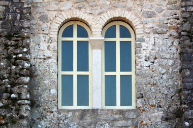 Krem rengi ahşap çerçeveli iki uzun, kavisli pencere ve çapraz mulyonlar, geleneksel duvar ve mimari simetri sergilenen, kalın, yıpranmış taş bir duvara yerleştirilmiştir.