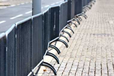 Bir yol kenarındaki kaldırımda kaldırım taşları düzgün bir şekilde dizilmiş, kentsel organizasyon ve kamu güvenliği önlemlerini vurguluyor.