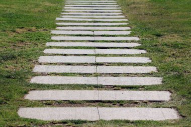 Dikdörtgen beton basamaklar düz bir çizgide eşit aralıklarla bir yol oluşturur yemyeşil bir çimenlikte, manzaralı bir bahçede görsel ritim yaratır.