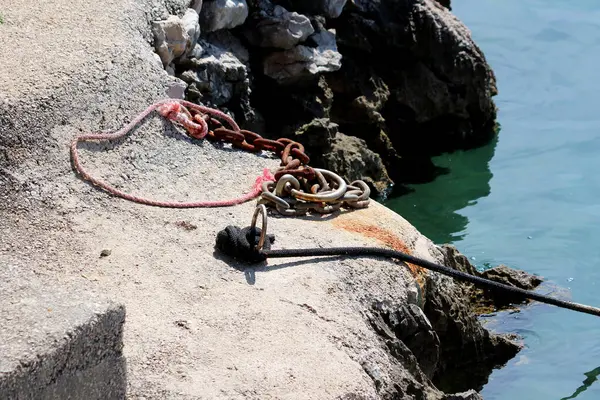 Demir halkalarla bağlanmış ağır çelik zincirler ve yıpranmış halatlar engebeli bir kıyı şeridinde beton bir iskelenin üzerinde uzanır. Aktif demirleme ya da kenetlenme olduğunu gösterir.