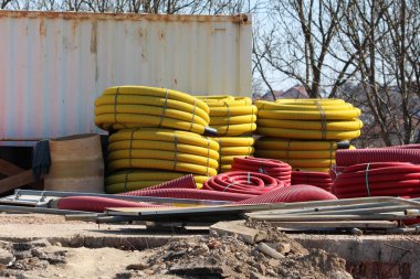 Parlak sarı ve kırmızı kıvrımlı elektrik hatları, bir yol şantiyesindeki dağınık malzemelerin arasına yerleştirilmek üzere büyük bobinler halinde istiflenmiştir.