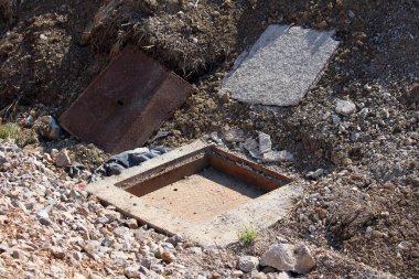 Ağır metal ve beton kapağı çıkarılmış, kısmen gömülü beton bir malzeme odası, iç kısımları bir yol inşaatı alanının yakınındaki kayalık bir yamaçta yer alıyor.