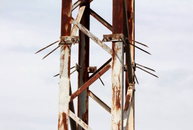 Çelik elektrik iletim kulesinin tabanında paslanma, sürgülü çapraz bağlar ve izinsiz girişi engellemek ve güvenliği sağlamak için tırmanma engelleri görünüyor.