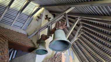 Açığa çıkmış kirişler, tuğlalar ve geleneksel kil kiremitlerle çevrili çatıdaki ahşap çan kulesinde iki eski bronz kilise çanı asılı duruyor.