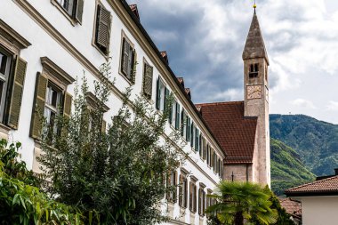 Kilise bitkilerle ve tipik güney tirol bitkileriyle çevrilidir. Arka planda yerel dağları genişletiyoruz.