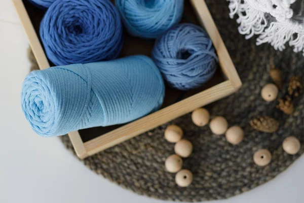 Composition of blue balls of thread in a wooden box, wooden necklace and cones on a white table. High quality photo