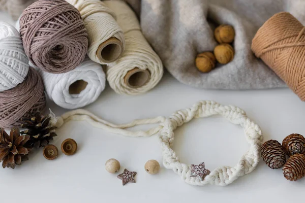 A composition of knitted gray sweater, knitting balls, cones, nuts, wooden beads and a white macrame wreath on a table. High quality photo