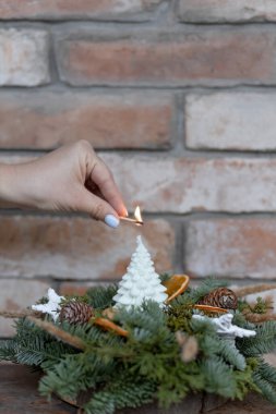 Bir kadın, Noel ağacı şeklinde bir mum yakar. Etrafında Noel eşyaları vardır. Duvarın arkasında. Yüksek kalite fotoğraf