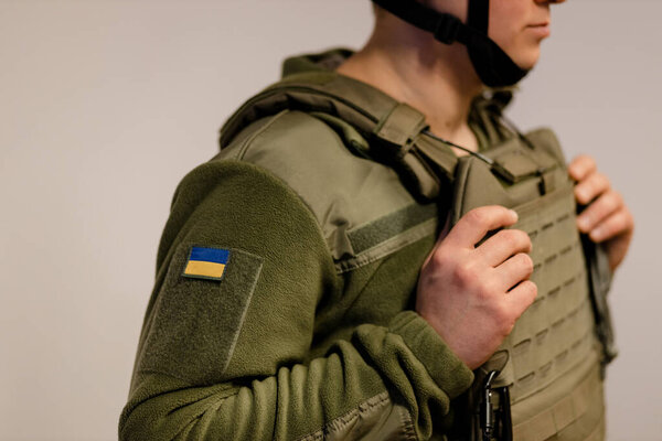  Armed Forces of Ukraine. Ukrainian soldier stands and holds hands on body armor. Ukrainian army. Ukrainian flag on military uniform.