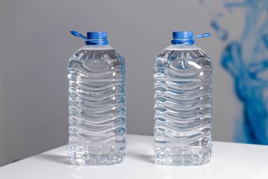 Two full 5 liter bottles of water on a white table on a gray background. Water delivery. High quality photo