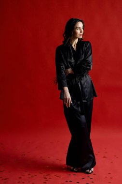 Fashionable European woman in a black suit on a red background looks away. Fashion, style, business woman. High quality photo