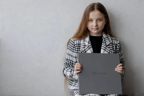 一个10岁的女孩正坐在那里 手里拿着一本印有记忆指纹的灰色真皮相册 看着摄像机 — 图库照片