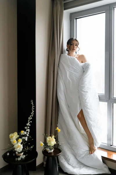 Beautiful Young Woman Wrapped Soft Blanket Stands Window Next Flowers — Stock Photo, Image