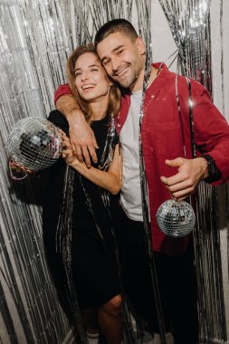  Genç ve romantik Avrupalı çift kameraya bakıp gülümsüyor, ellerinde disko toplarını gümüş perde arkasında tutuyorlar. Yüksek kalite fotoğraf