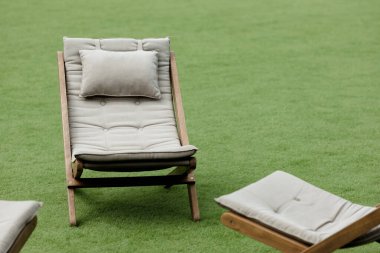 Serin yeşil bir çimenliğe yerleştirilmiş rahat bir şezlonga sahip sakin bir sahne. Tasarım ve metin için bolca kopya alanı var. Güneşli bir günde rahatlamak ve dinlenmek için mükemmel bir yer..