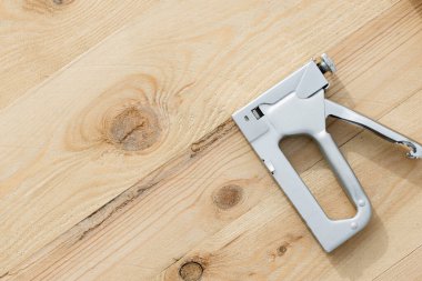 Gümüş bir zımba tabancası ahşap bir yüzeye dayanır. Metal ve ahşap arasındaki kontrastı vurgular..