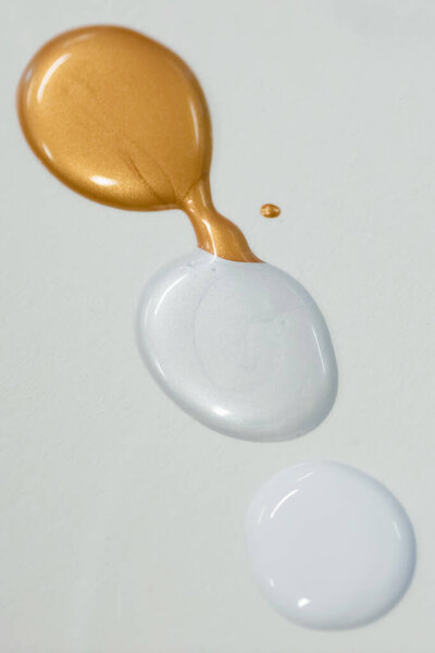Three distinct drops of liquid, one golden and two clear, elegantly placed on a white surface.