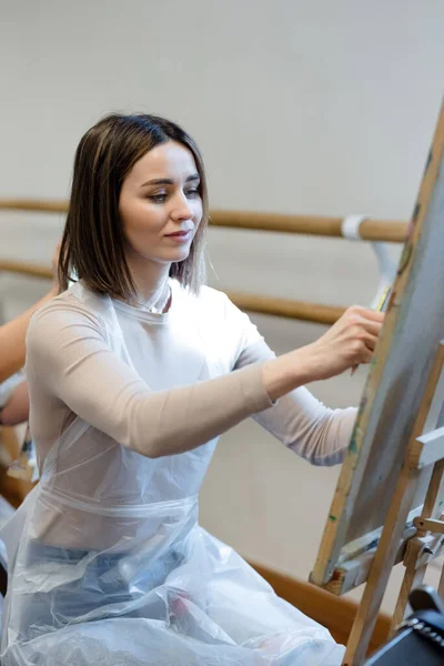 An artist, covered with a clear plastic sheet, is deeply focused on painting on a canvas in a serene studio.