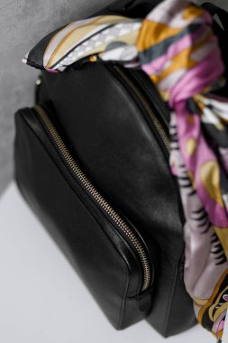 Şık siyah deri bir çantanın yakın çekimi, canlı, çok renkli bir eşarpla süslenmiş. Resim torba dokusunu ve eşarp tasarımını vurguluyor