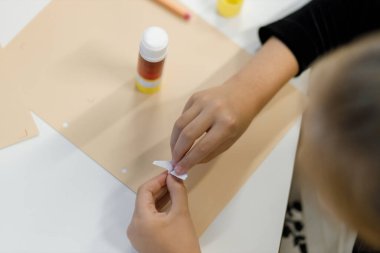 Çocuk ellerinin yaratıcı bir zanaat faaliyetiyle odaklanmış nişanını yakalayan bir görüntü. Gösterilen bariz dalma ve marifet gençlik hayal gücünün ve yaratıcılığın özünü temsil ediyor.