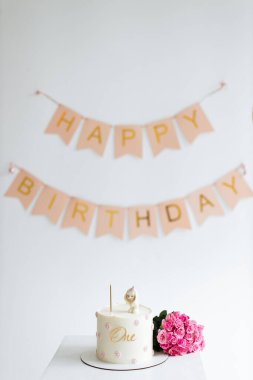 Hoş bir şekilde düzenlenmiş bir ilk doğum günü kutlaması dekoru, bir numaralı doğum günü afişi, bir numaralı pasta ve bir buket canlı pembe çiçek..