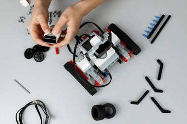 Eller, bir teknoloji atölyesindeki temiz bir tezgahta çeşitli parça ve aletler kullanarak bir robot arabası monte ediyor. Kurulum tekerlekleri ve özelleştirme için diğer bileşenleri içerir.