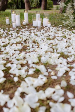 Gece boyunca yumuşak bir ambiyans oluşturan parlayan mumlarla çevrili, yere saçılmış beyaz çiçek yapraklarıyla süslenmiş sakin bir dış mekan..