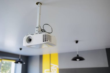 Çağdaş bir çalışma alanının tavanından sarkan parlak bir projektör. Yumuşak ışıklandırma odayı aydınlatır. İşbirliği ve öğrenme için mükemmel bir atmosfer yaratır..