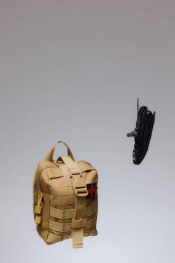 Açık hava maceraları ve acil durum hazırlıkları için gerekli teçhizatı vurgulayan siyah bir turnike yanında parlak kırmızı bir haç ile bronz bir ilk yardım kiti belirgin bir şekilde sergilenmektedir..