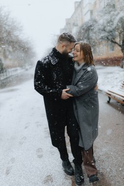 Bir çift, taze karla kaplı büyüleyici bir sokakta şefkatli bir kucaklaşmayı paylaşıyor. Flake 'ler etraflarında dans ederek, samimi atmosferi güçlendirir. Neşe ve sıcaklık soğuk havayı doldurur..