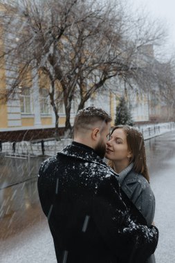 Tuhaf, karla kaplı bir sokakta, iki birey, nazikçe düşen kar taneleri ve birbirlerinin sıcaklığıyla çevrili hassas bir anı paylaşıyor. Neşeleri serin arka planda yayılıyor.