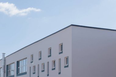 Pürüzsüz, minimalist bir bina parlak mavi bir gökyüzüne karşı duruyor. Temiz çizgiler ve geometrik şekillerle..