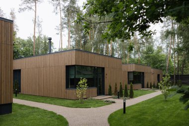 Ağaçlar ve yeşil peyzaj ile çevrili büyük pencereli modern ahşap ev ve minimalist tasarım