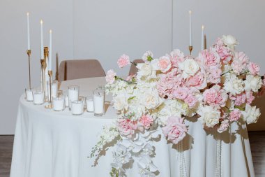Güzel dekore edilmiş bir masa, parlak mumlarla hafifçe aydınlatılmış bir dizi pembe ve beyaz çiçek sergiliyor. Düzenleme, kutlama atmosferine cazibe ve sıcaklık katıyor..