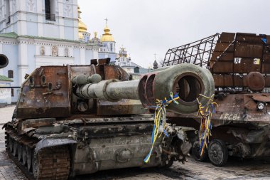 A burned-out russian self-propelled gun against the backdrop of the Golden Dome Cathedral in Kyiv with tied yellow-blue ribbons.
