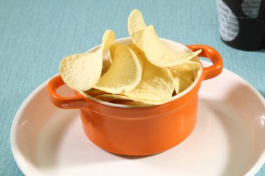 Beyaz tepside turuncu bir kasede tuzlanmış patates cipsi. 