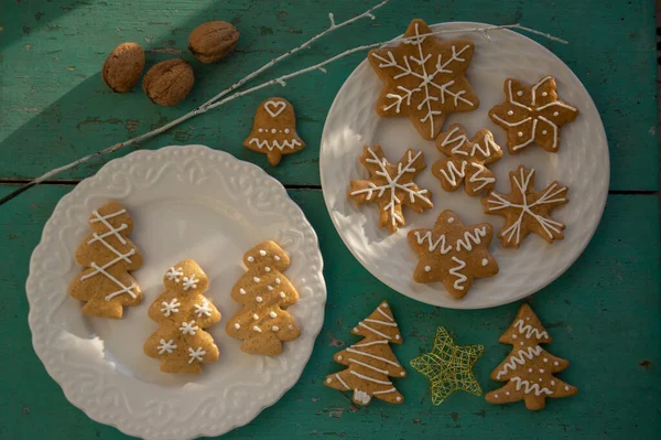 stock image Painted traditional Christmas gingerbreads arranged on white plates on old vintage painted table in daylight, various xmas shapes trees, stars and snowflakes