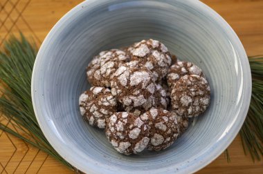 Lezzetli kırışıklıklar, kahverengi ve beyaz çikolata aromalı kakao aromalı buruşuk kurabiyeler mavi kasede pudra şekerle kaplı bambu ahşap arka planda.