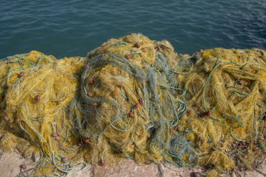Fishermans equipment lying on the coastline in harbor, heap nylon yellow tangled fishing net in greece sunlight