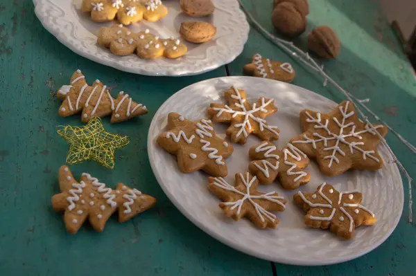 stock image Painted traditional Christmas gingerbreads arranged on white plates on old vintage painted table in daylight, various xmas shapes trees, stars and snowflakes