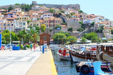 Arka planında Bizans şatosu olan Kavala 'nın eski kasabası ve ön tarafındaki sahil geçidinde palmiyeler ve yayalar. Kavala kasabası, Makedonya, Yunanistan.