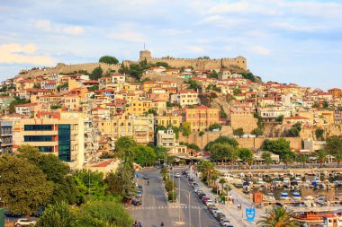 Arka planında Bizans şatosu olan Kavala 'nın eski kasabası, sokağın yanında modern tarz evler ve önünde balıkçı tekneleri olan liman. Kavala kasabası, Makedonya, Yunanistan. 