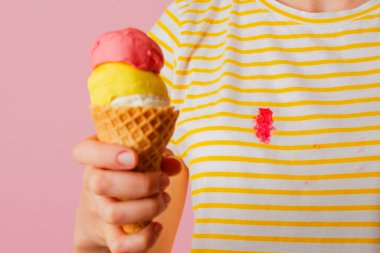 Kıyafetlerin üzerine kremalı çilekli dondurma dökmek. Pembe arka planda üç kepçe farklı aromalı dondurma külahını tutan bir kız. İzole. Yüksek kalite fotoğraf