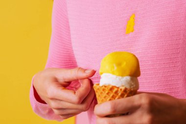 Kadın eli bluzunda lekeli, muzlu, kremalı dondurmayı gösteriyor. İzole. Sarı arka planda. Yüksek kalite fotoğraf