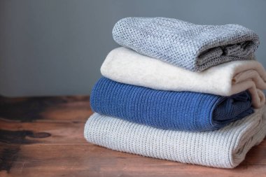 Ahşap bir arka planda kışın örülmüş kazak yığını. Mevsim ve gardırop değişikliği. Sürdürülebilir ve ekolojik moda. Yüksek kalite fotoğraf