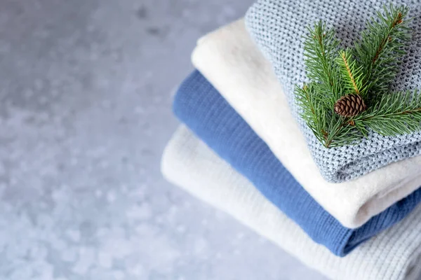 stock image A stack of clothes with sweaters decorated with a Christmas tree branch with a cone on a gray background. top view. . High quality photo