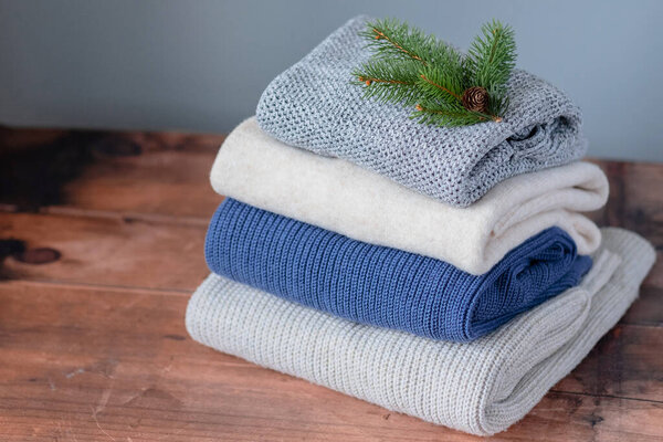 A stack knitted sweaters decorated Christmas tree branch with a cone on a wood background. High quality photo