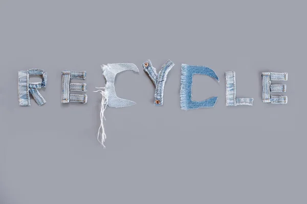 Recycle word from denim jeans and destroyed denim torn shreds, on a gray background. Denim Recycling. Textiles and clothing Sustainability. High quality photo