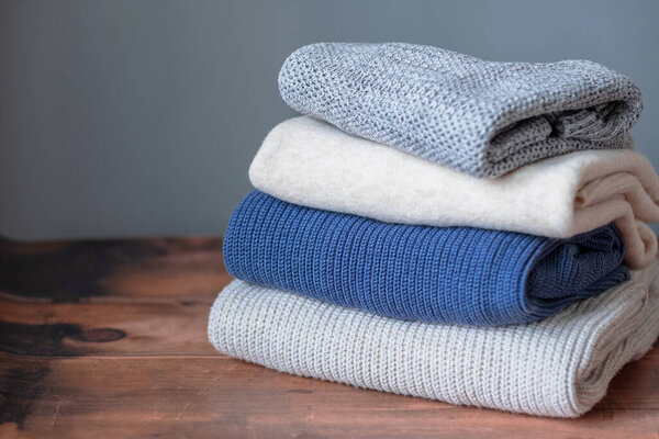 A stack winter warm knitted sweaters on a wooden background. Change of season and wardrobe. Sustainable and ecological fashion. High quality photo